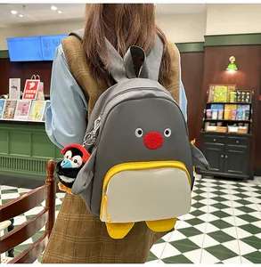 Détail d'un sac à dos pingouin gris avec breloque en peluche et poche zippée jaune vif