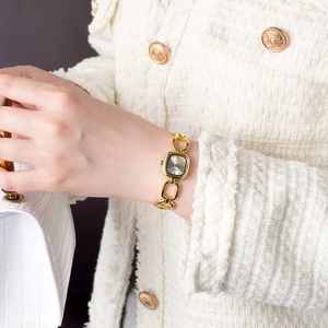 Elegant gold bracelet watch with rectangular dial worn with luxury tweed jacket