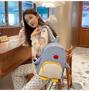Détail du sac à dos pingouin mignon bleu et jaune porté par une étudiante dans un café