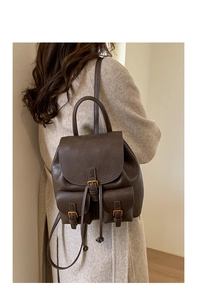 Close-up of vintage dark brown leather backpack with buckle pockets worn by a model
