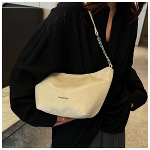 Detail of cream leather underarm bag with metal logo and chain strap on a model