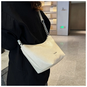 Detail of matte cream underarm bag with silver chain strap and metal logo plaque