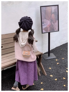 Vue arrière d'un enfant portant un mini sac en cuir marron avec nœud dentelle dans un parc