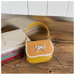 Détail macro du mini sac jaune avec rabat en daim marron et décoration de nœud argenté