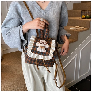 Detail of kids brown checkered backpack featuring plush dog and white lace trim