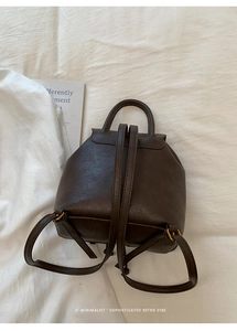 Flat lay of vintage dark brown faux leather backpack with top handle and gold buckles