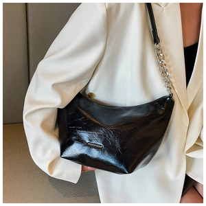 Detail of black glossy leather underarm bag featuring metal chain strap and logo plaque