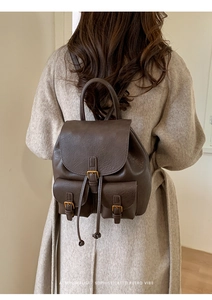 Retro dark brown leather backpack on model wearing a beige coat from a back view