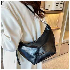 Side view of black glossy crescent underarm bag with silver chain worn on white coat