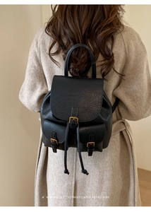Detail eines schwarzen Retro-Lederrucksacks mit goldenen Schnallen, getragen zu einem Mantel