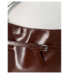 Detail of dark red glossy PU leather shoulder bag with silver buckle and belt feature