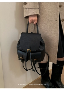 Close-up of black leather backpack with gold hardware buckles and minimalist front pockets