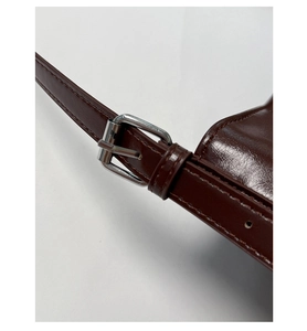Detail of dark brown glossy PU leather strap with silver metal adjustable buckle