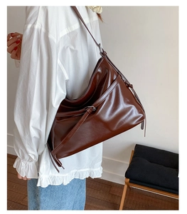 Detail view of large dark brown shiny PU leather tote bag worn on shoulder by model