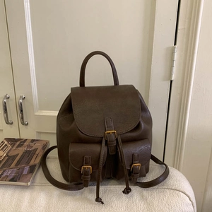 Detail of dark brown faux leather backpack with gold buckles and vintage flap pockets
