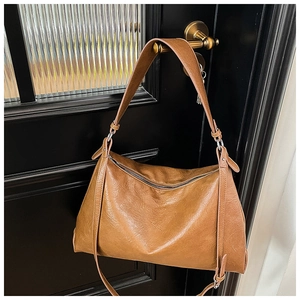 Detailed view of caramel leather tote bag hanging on a gold handle with metal zipper