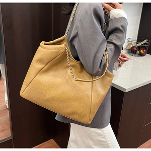 Detail of a khaki textured leather tote bag with metal chain strap on a model's shoulder