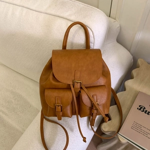 Detailed view of vintage caramel brown PU leather backpack with buckle straps on a white sofa