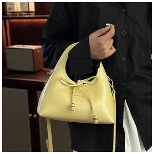 Close-up of pale yellow glossy leather bag featuring bow ties and silver bead charms