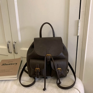 Detail view of dark brown faux leather backpack featuring pebbled texture and metal buckles