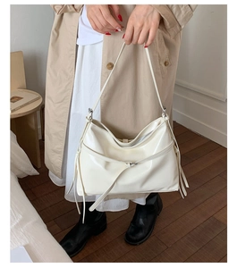 Close-up of beige PU leather tote bag with stylish side tassel detail on model outfit