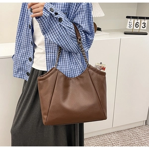 Detail view of large brown pleated leather tote bag with silver chain straps on model