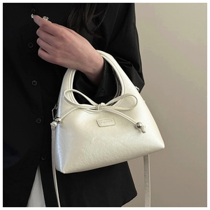 Detailed close-up of white leather handbag featuring bow knot and silver metallic charms