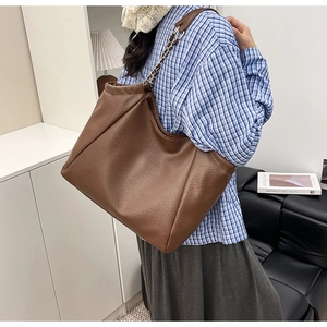 Detail of dark brown tote bag with metal chain strap worn on shoulder in a home setting