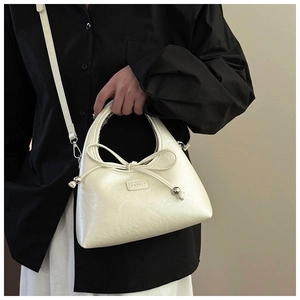 Detail view of a cream mini handbag with a decorative bow and adjustable strap worn on person