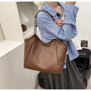 Brown lychee textured tote bag with chain leather strap shown on a model in a minimalist room