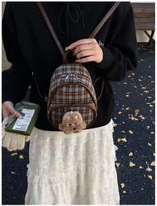 Close-up of a mini plaid children backpack with a cute plush bear charm and metal zipper