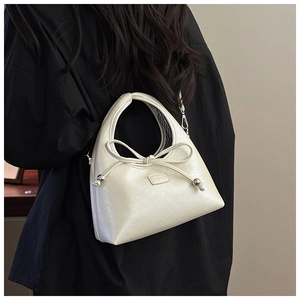 Detail of cream leather shoulder bag featuring ribbon bow and black striped lining
