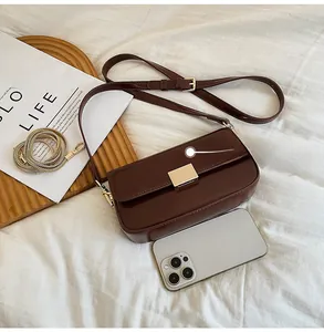 Detail of dark brown leather crossbody bag with gold buckle and metal chain strap