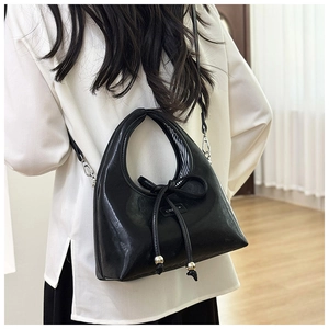 Detail of minimalist black PU leather shoulder bag with decorative bow and metal beads