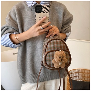 Detail of a vintage plaid mini backpack with a plush puppy pendant and pearl collar