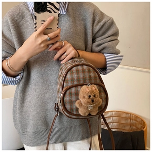 Detail of green plaid mini backpack with brown leather trim and plush puppy charm