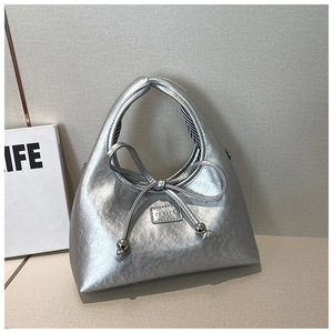 Detail of silver metallic underarm bag with bow drawstring and branded metal plaque