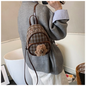 Close-up of a mini plaid backpack for kids with a cute plush bear charm on the zipper