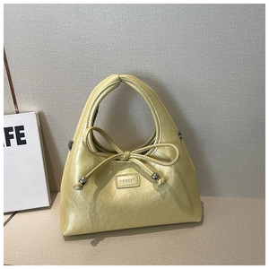 Detail of light yellow leather bag with decorative bow and silver metal sphere accents