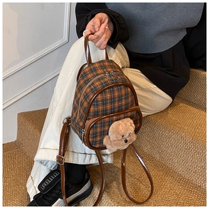 Detail of brown plaid tweed mini backpack featuring a plush teddy bear ornament and dual zippers