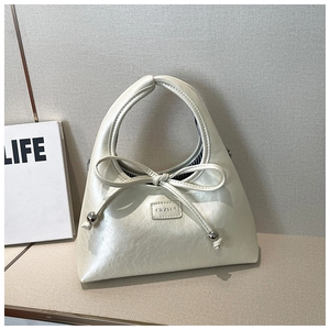 Detail of cream hobo bag featuring a leather bow knot and silver metallic bead accents
