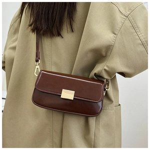 Detail of dark brown polished leather shoulder bag with gold clasp on khaki coat