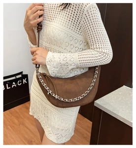 Détail d'un sac demi-lune en daim marron avec chaîne argentée et fermeture éclair fluide