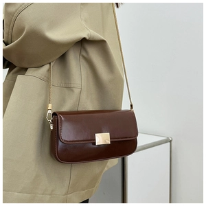 Detail of dark brown leather crossbody bag with gold buckle and chain on model