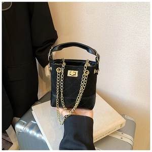 Detail of black quilted bucket bag featuring gold metal lock and chain strap for children