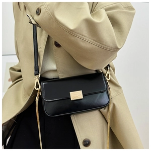 Detail of minimalist black square bag with gold metal buckle and dual strap on beige coat