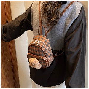 Detail of plaid mini backpack featuring brown leather straps and cute plush bear charm