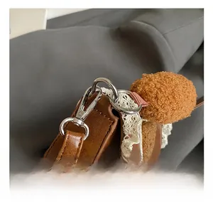 Detail of silver metal hook, brown faux leather texture and beige lace on handbag