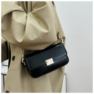 Detail of a black square crossbody bag with gold buckle and chain strap on a trench coat