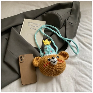 Handmade knitted brown bear mini crossbody bag with blue birthday hat on soft fabric